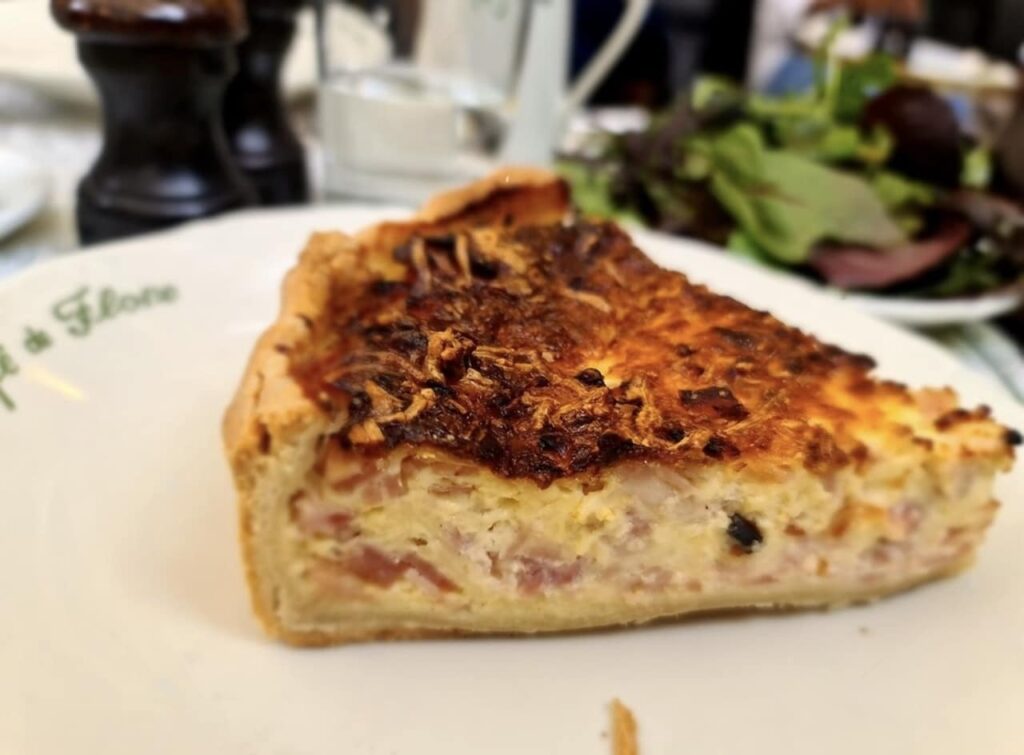 A slice of Quiche Lorraine, a renowned dish among famous French foods, with a golden-brown crust and a savory filling, served on a plate with a side salad, capturing the essence of French cuisine.