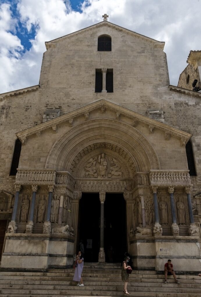 Visitors ascending the steps to the imposing entrance of Saint-Trophime Church in Arles, showcasing intricate carvings and historical artistry, a must-see destination for those compiling the best things to do in Arles.