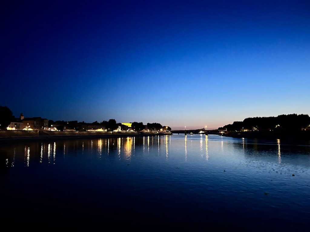 Twilight descends over the Rhône River in Arles, with lights reflecting on the water's surface, a tranquil scene reminiscent of 'Starry Night Over the Rhône' and a peaceful experience for visitors exploring the best things to do in Arles.