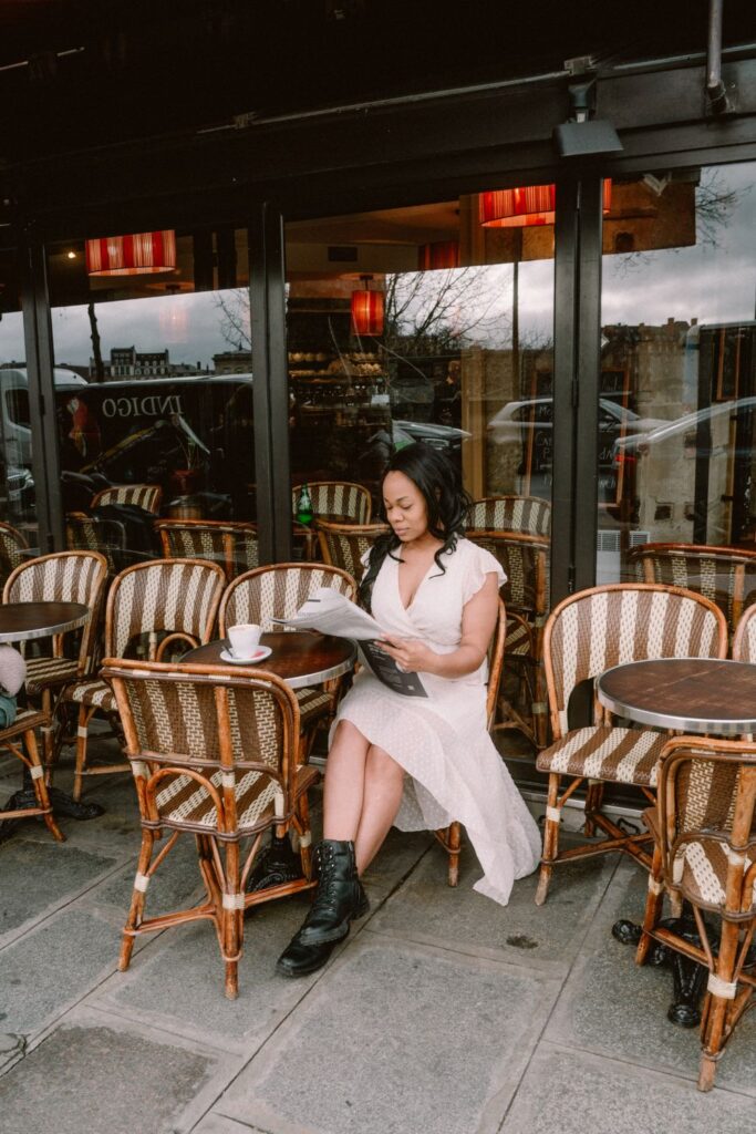 A woman engrossed in reading a menu at a quintessential Parisian café terrace, wearing a white dress paired with black combat boots, capturing a relaxed yet fashionable moment at one of Paris instagram spots.