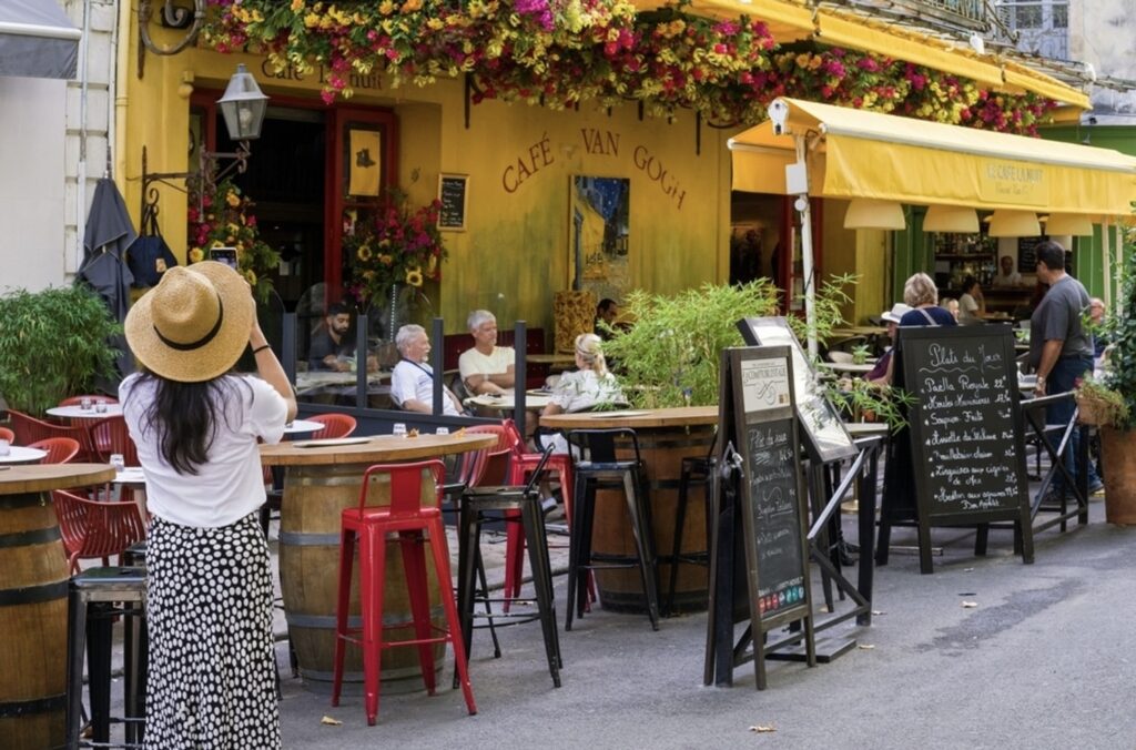 The iconic Café Van Gogh in Arles, vibrant with yellow walls and adorned with bright flowers, as patrons enjoy outdoor seating, capturing the essence of the scene immortalized by Van Gogh, a picturesque spot among the best things to do in Arles.