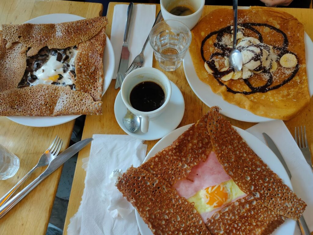 A feast of famous French foods with savory and sweet crepes: one filled with ham and egg, another with chocolate and banana, accompanied by a cup of black coffee, embodying the versatile and delightful nature of French creperies.