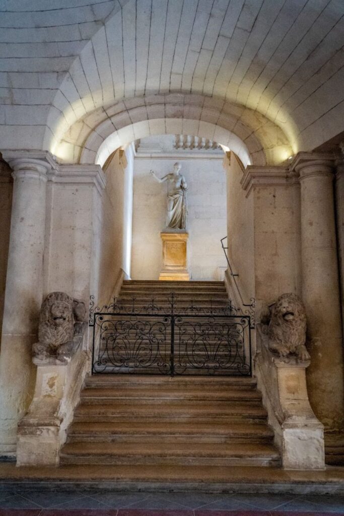 Sculpture of a robed figure atop a grand staircase flanked by stone lion sculptures, within the atmospheric Cryptoportiques d'Arles, a must-visit for history enthusiasts exploring the best things to do in Arles.