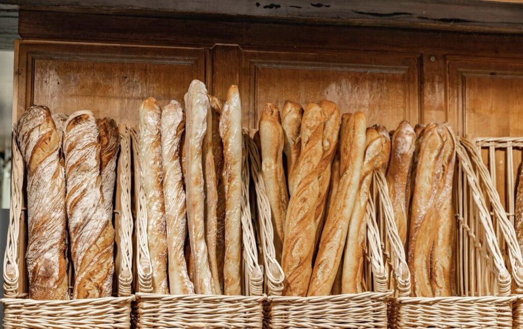 A selection of freshly baked baguettes, a symbol of famous French foods, displayed in wicker baskets against a vintage wooden cupboard, highlighting the artisanal tradition and charm of French bakeries.