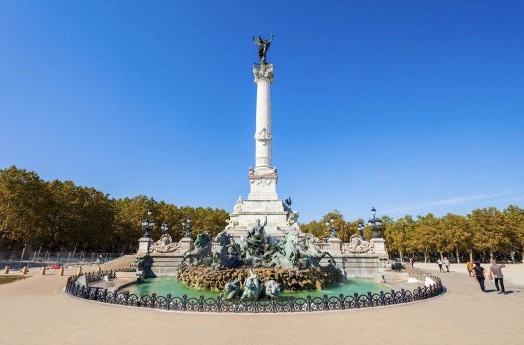 The Monument aux Girondins stands tall against the blue sky in the Place des Quinconces in Bordeaux, with its impressive column and fountain sculptures, a testament to the city's rich history and a prominent feature that draws visitors exploring the things to do in Bordeaux.