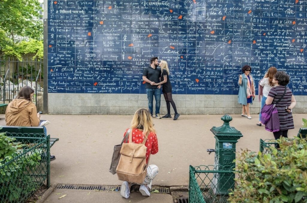 A couple embraces in front of the 'I Love You Wall' in Paris, where the phrase is featured in multiple languages, setting a multicultural romantic scene for Valentine's Day in Paris