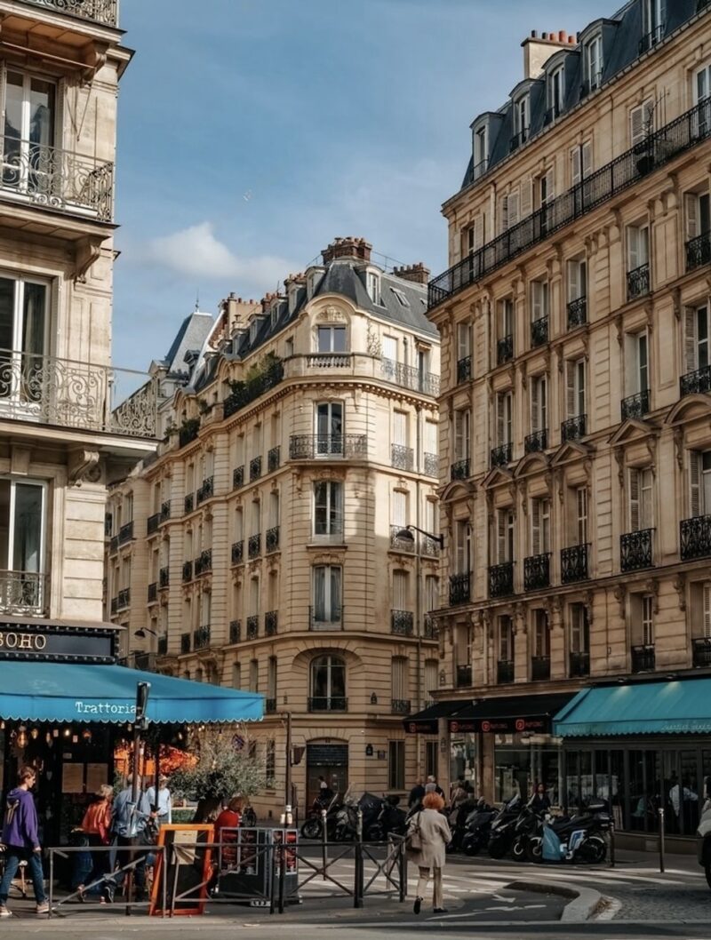 A vibrant street scene in a bustling neighborhood, with elegant Parisian buildings and a busy trattoria terrace, capturing the ambiance of the best arrondissement to stay in Paris for an authentic experience of the city's renowned culture and cuisine.