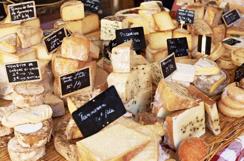An array of famous French cheeses, from creamy Brie to pungent Roquefort, artfully displayed at a market with descriptive signs, embodying the rich diversity and gastronomic pride of French food culture.