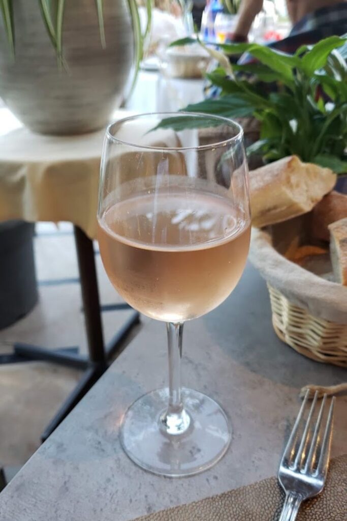 A chilled glass of rosé wine on a table at a cozy outdoor café in Nice, with a basket of fresh bread in the background, inviting a taste of the local lifestyle. An image that evokes the relaxed dining experience in Nice, perfect for a travel guide highlighting the region's culinary delights.