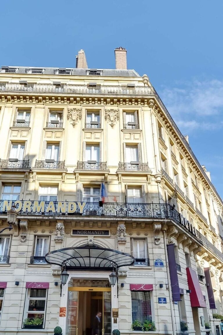 Facade of Hotel Normandy, one of the best 1st Arrondissement Paris hotels, featuring a historic building with ornate architecture and a prominent 'Normandy' sign, under a clear blue sky.