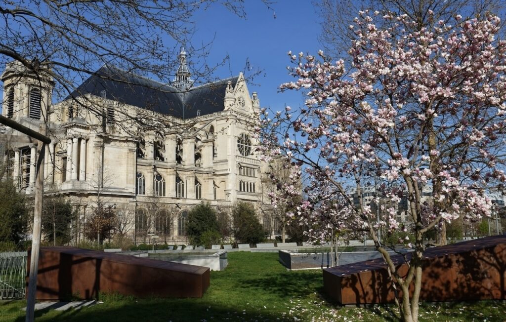 Église Saint-Eustache in the 1st arrondissement of Paris, framed by blooming trees and greenery on a sunny day, showcasing its impressive Gothic architecture.