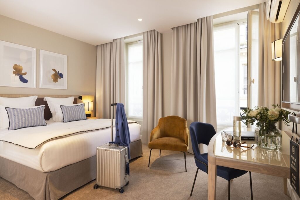 Stylish room at Hôtel Duminy Vendôme, one of the best hotels in the 1st Arrondissement of Paris, featuring a comfortable bed with decorative pillows, a cozy seating area, and a desk with flowers and travel essentials.