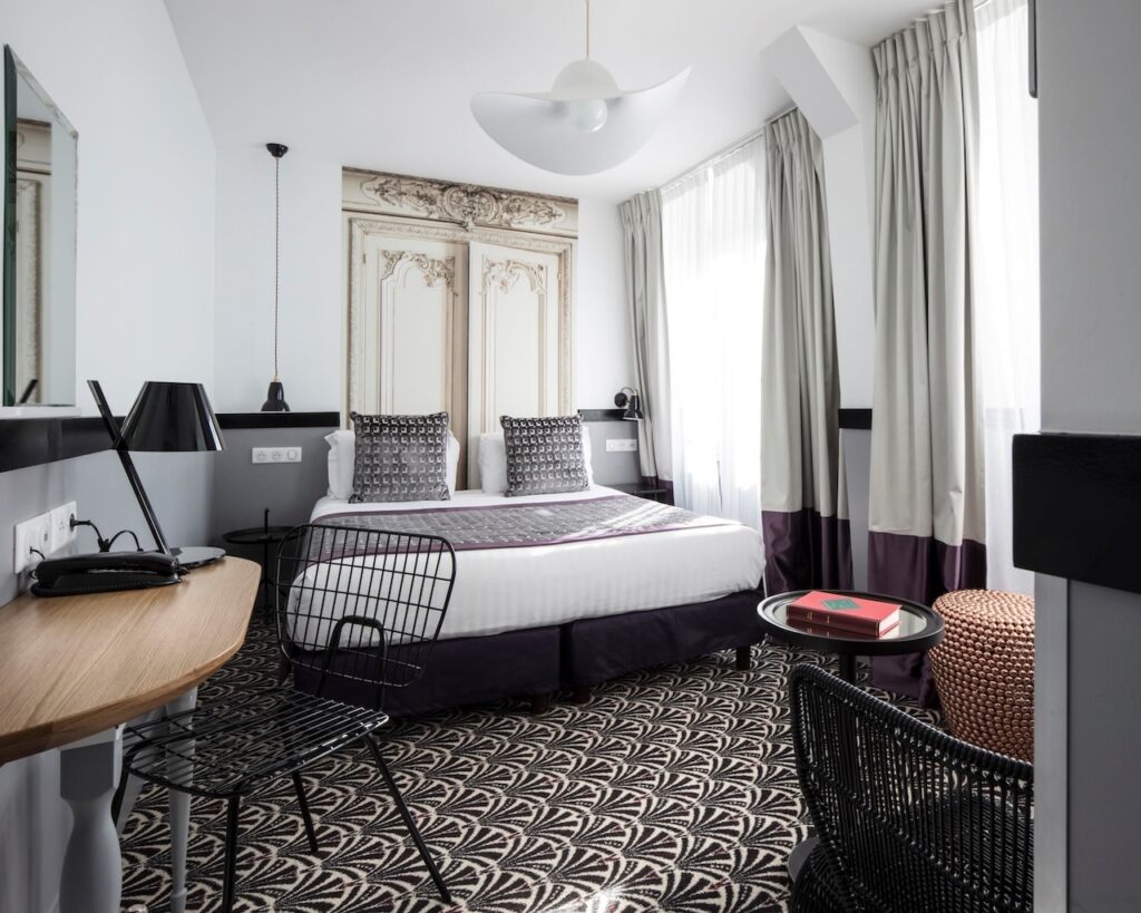 Chic room at Hôtel Malte - Astotel, considered one of the best 1st Arrondissement Paris hotels, featuring a modern design with a stylish bed, geometric-patterned carpet, and elegant furnishings including a work desk and seating area.