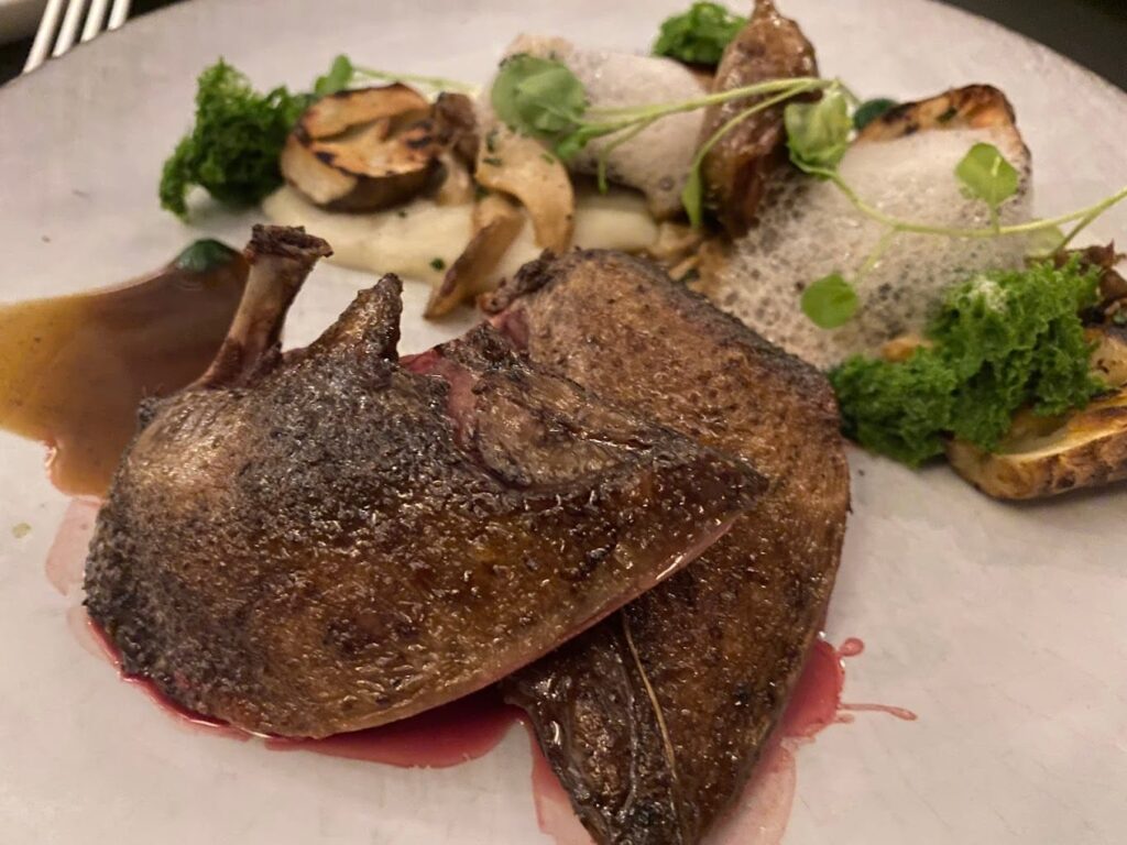 A gourmet dish from one of the best restaurants in Bordeaux, France, featuring perfectly cooked game meat, creamy mashed potatoes, and garnished with sautéed mushrooms, green herbs, and a delicate foam.