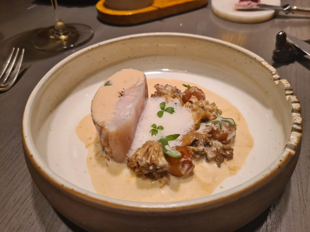 A refined dish from one of the best restaurants in Bordeaux, France, featuring a succulent piece of poultry accompanied by a creamy sauce, garnished with delicate herbs and paired with small, roasted vegetables.