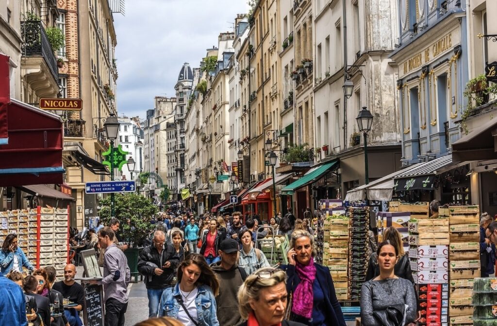 1st arrondissement in paris: a bustling street scene on Rue Montorgueil in Paris, filled with pedestrians and lined with shops, cafes, and market stalls. The atmosphere is vibrant with people shopping, dining, and walking along the narrow street.