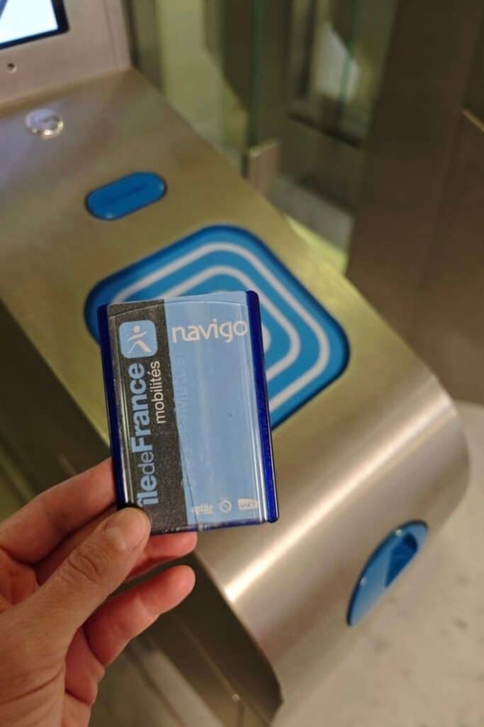 Holding a Navigo pass in front of a Paris Metro turnstile sensor, showing how to use the Metro in Paris with a contactless card.