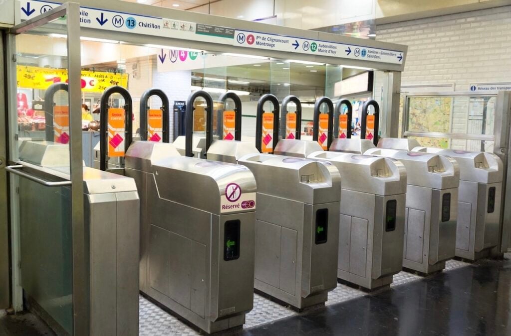 Entrance gates at a Paris Metro station, showing how to use the Metro in Paris with ticket validation and line directions overhead.