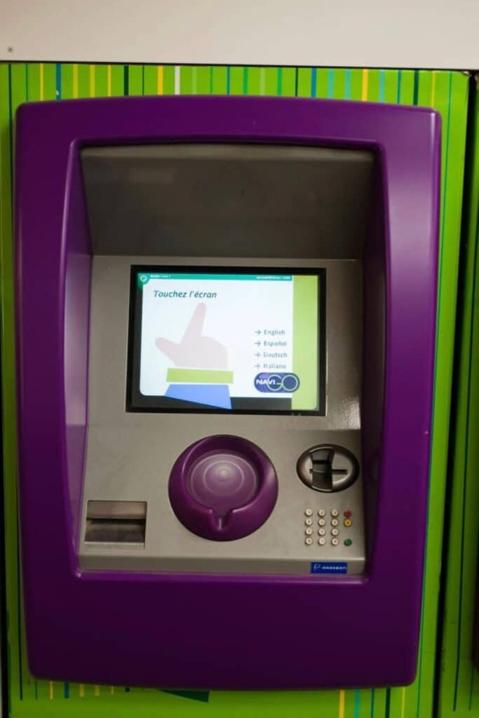 Close-up of a purple Paris Metro ticket machine touchscreen, showing how to use the Metro in Paris to buy tickets in multiple languages.